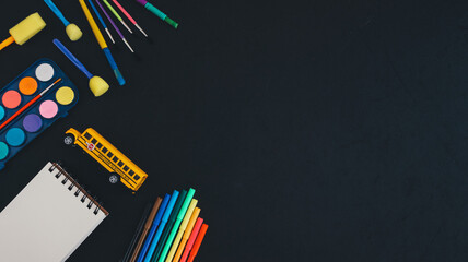 School bus and art supplies on black.
School bus, paints, pencils, brushes and markers lie on the left against a black background with space for text on the right, top view close-up.