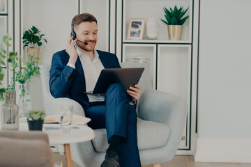 Happy young businessman in suit having pleasant online conversation on laptop