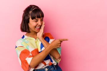 Young mixed race woman isolated on pink background saying a gossip, pointing to side reporting something.