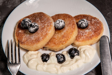 Healthy breakfast of cottage cheese pancakes, syrniki with blueberries and sour cream close-up in a plate on the table. Traditional Russian / Ukrainian cuisine, breakfast
