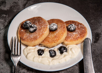 Healthy breakfast of cottage cheese pancakes, syrniki with blueberries and sour cream close-up in a plate on the table. Traditional Russian / Ukrainian cuisine, breakfast