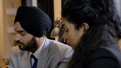 Closeup of two Indian businesspeople, one from the Sikh religion, one a woman, in a meeting indoors