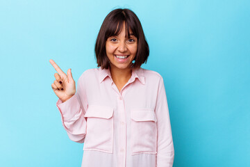 Young mixed race woman isolated on blue background smiling cheerfully pointing with forefinger away.