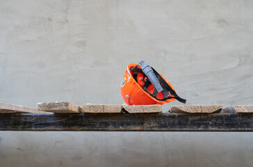 An orange plastic construction helmet lies on the wooden planks of the scaffolding. A wall with fresh gray plaster is visible in the background. Background. Texture.