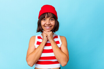 Young mixed race woman isolated on blue background keeps hands under chin, is looking happily aside.