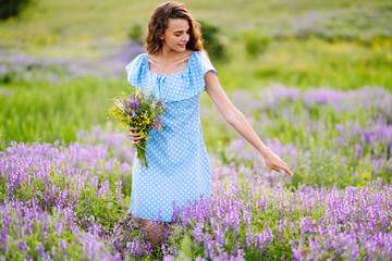 Young woman in stylish summer dress feeling free in the field with flowers in sunshine. Nature, vacation, relax and lifestyle. Summer landscape.