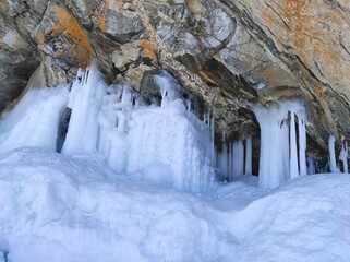 rocks covered with snow and icicles near a lake covered with ice