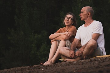 portrait of a couple senior man and woman sitting on the beach at sunset time in summer