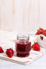 Jar of strawberry jam on wooden rustic board.