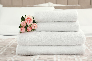 Fototapeta na wymiar Stack of fresh towels with flowers on bed indoors