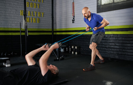 Personal Trainer Holding Resistance Bands. Mature Man Does Bicep Curl