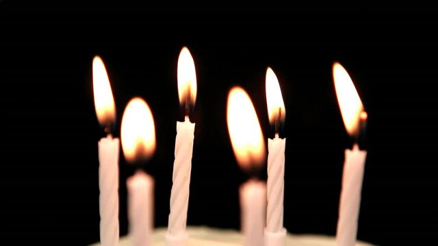 Animation of red kaleidoscopic shapes moving over lit birthday cake candles, blown out, on black