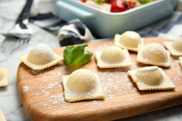 Raw ravioli with basil on wooden board, closeup