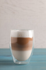 Glass of delicious layered coffee on turquoise wooden table against white background, space for text