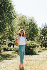 Charming fashionable young woman in glasses and hat with handbag on her shoulder carelessly walking...
