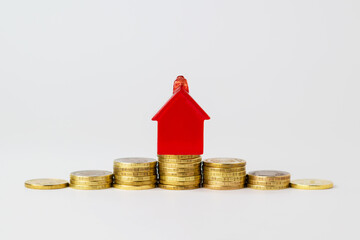 A small, red toy house stands on a pyramid of yellow, gold coins. The concept of economic growth of profits in the real estate market, mortgages and capital. Isolated on white background.