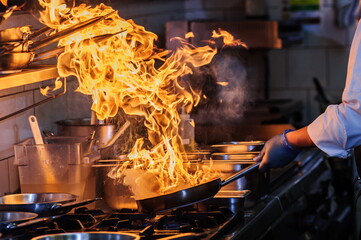 Chef is stirring vegetables in wok on open fire