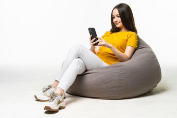 Young woman with mobile phone sitting on beanbag chair against on white background