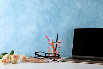 Comfortable workplace with modern laptop, stationery and flowers near light blue wall. Space for design