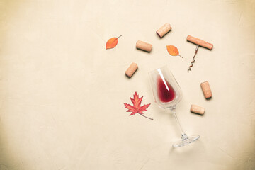 Glass of red wine with corks and corkscrew flat lay on beige concrete background. Autumn still life with wine and dry leaves. Top view.