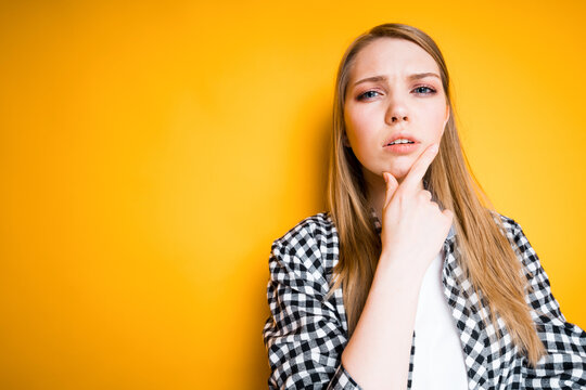A beautiful girl in a shirt thoughtfully touches her chin with her hand while thinking about something