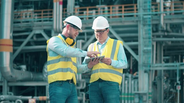 Oil refinery engineers are using a tablet while discussing plans