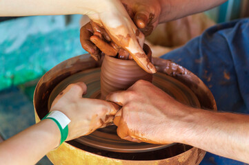 Potter makes on the pottery wheel clay pot and conducts a master class. Hands of the master and child close-up during work. Ancient national craft