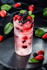 Fresh berries cocktail with raspberry, blackberry, mint and ice in jar glass on dark black background. Summer cold drink and cocktail.