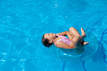a joyful five-year-old girl floating cross-legged and eyes closed on a blue inflatable circle at the sea or in the pool, with copy space. 