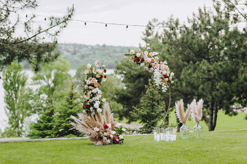 A beautiful, round wedding arch, decorated with flowers, roses, reeds, glass candlesticks with...