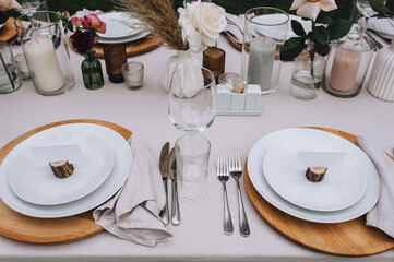 A set of various dishes and accessories on a wooden table with a tablecloth - plates, forks, knives, glasses, roses in vases, candles in candlesticks.