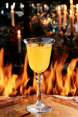 Yellow cocktail in a beautiful goblet glass on copper designer bar counter, the background of real fire. autumn cocktail. Series of photo. High quality photo