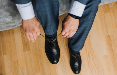 A man, a businessman, ties his shoelaces with his hands on shiny black leather shoes. Wedding portrait of the groom in the morning. Preparation for work.