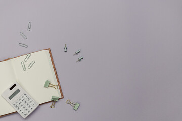 Back to school creative concept. Study or office workplace with stationary like notebook,  calculator and clips on a purple paper background.  Minimalistic flat lay, top view with copy space.