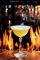 Yellow cocktail with foam in a beautiful goblet glass on copper designer bar counter, the background of real fire. cocktail with egg white. Series of photo. High quality photo