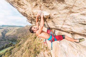 Climber grimacing as he holds on with both hands on the rock