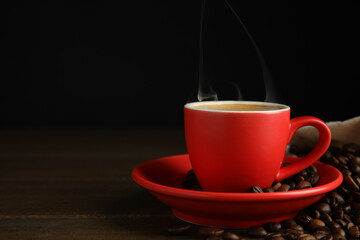 Cup of tasty coffee and beans on wooden table, space for text