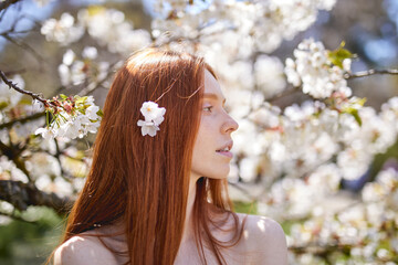 Naklejka premium Potrait of young woman being relaxed standing among blooming spring trees. Female enjoys spring and smells flowers on trees. Season change and fresh day concept