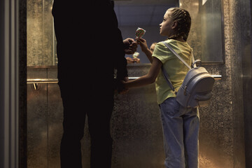 Rear view on unrecognizable man with child standing in lift, elevator, view from back. man give...