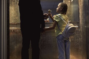 Obraz premium Rear view on unrecognizable man with child standing in lift, elevator, view from back. man give candy. little girl is very gullible, don't afraid of adult man, holding hands together