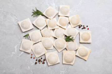 Uncooked ravioli, rosemary and peppercorns on grey marble table, flat lay