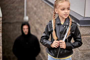suspicious man is following girl in city street. Abduction of children. Trafficking, man Spying on child girl in the background. focus on blonde child in leather jacket. Harassment and assault - obrazy, fototapety, plakaty
