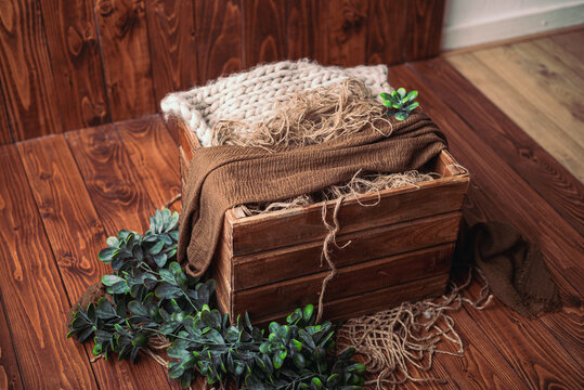 Basket on a wooden floor. Props for newborn photography. Brown basket with dark green branch. Newborn photography backdrop