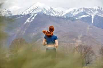 Fototapeta na wymiar Rear view On Redhead Sporty Female Jogging Among Mountains, Enjoy Workout In The Morning, In Sportive Wear, Run Forward. View From Back