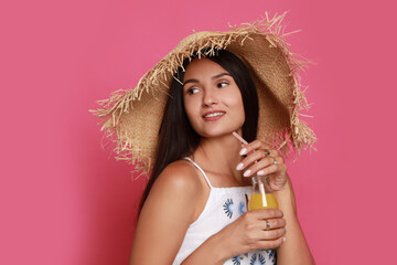 Beautiful young woman with straw hat and bottle of refreshing drink on pink background