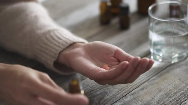 Woman takes a pill. Three pills fall into the palm of a woman from a bottle of pills. A woman's hand is taking pain reliever, pain medication. Close-up. Home, healthcare and medicine treatment concept