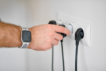 Hand ready to plug or unplug black power cord cable Into electric socket on wall. Ready to connect...