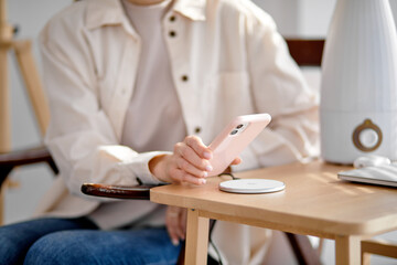 Charging mobile phone battery with wireless charging device on table, close-up hands. Smartphone charging on charging pad. Mobile phone near wireless charger. Copy space - obrazy, fototapety, plakaty