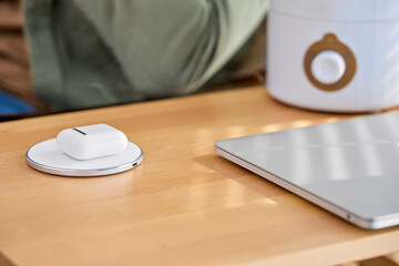 Close-up Charging Headphones Using Wireless Charging Pad At Home, Copy Space, On Table With Laptop, Modern Technologies And Smart House Concept.