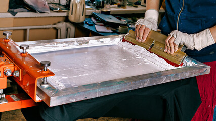 selective focus photo of male hands with a squeegee. serigraphy production. printing images on...